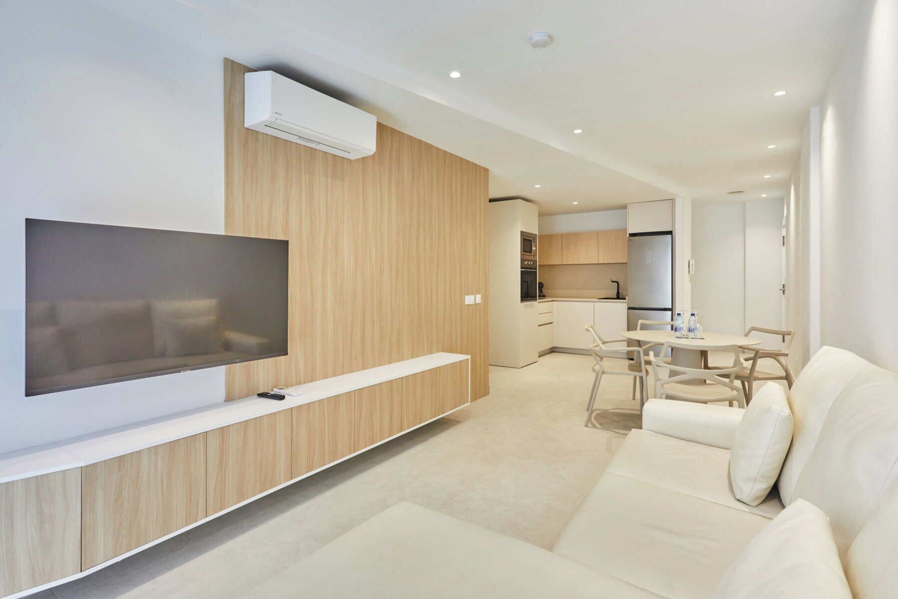Een moderne woonkamer met een flatscreen televisie, een bank en een eethoek met stoelen.