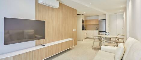 Una sala de estar moderna con una televisión de pantalla plana, un sofá y una zona de comedor con sillas.