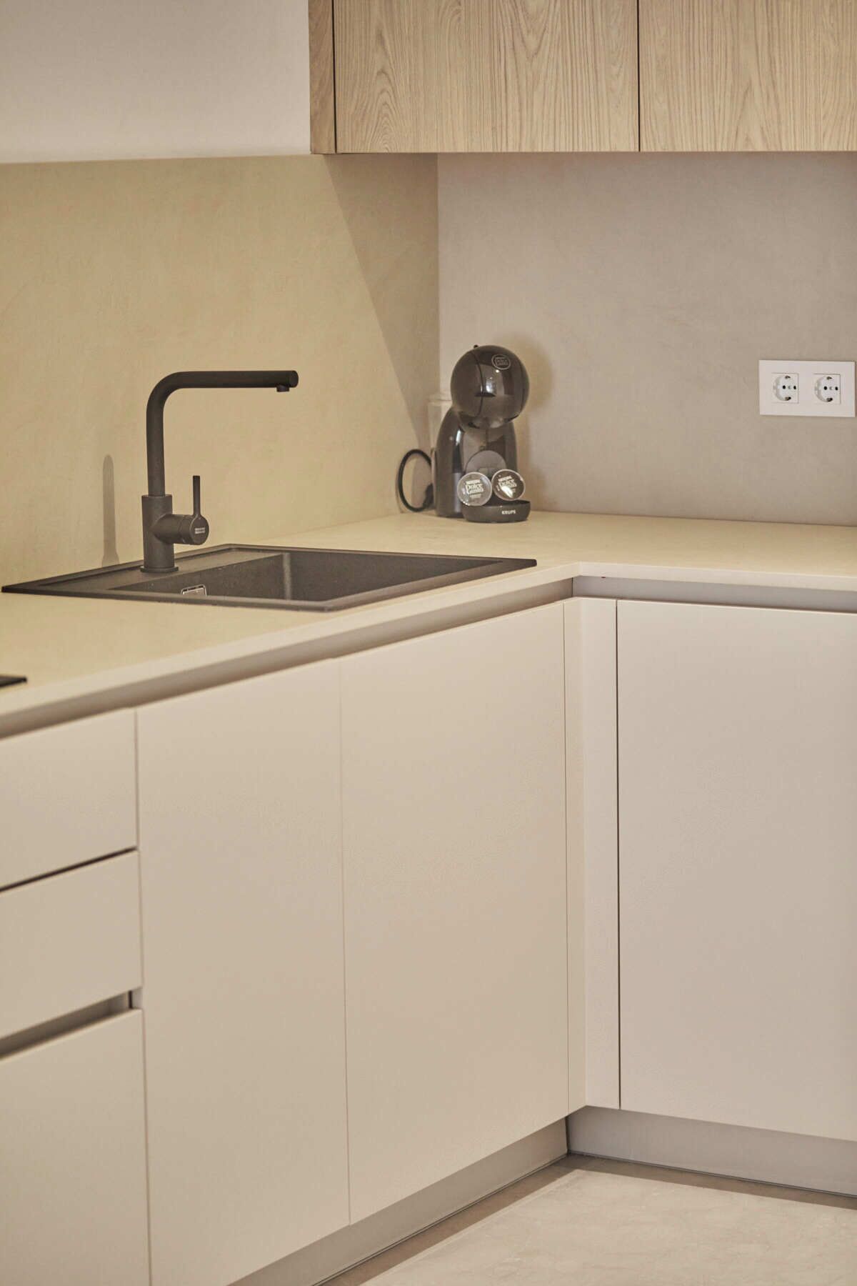 A kitchen with a modern design, featuring a sink, a coffee machine, and light-colored cabinets.