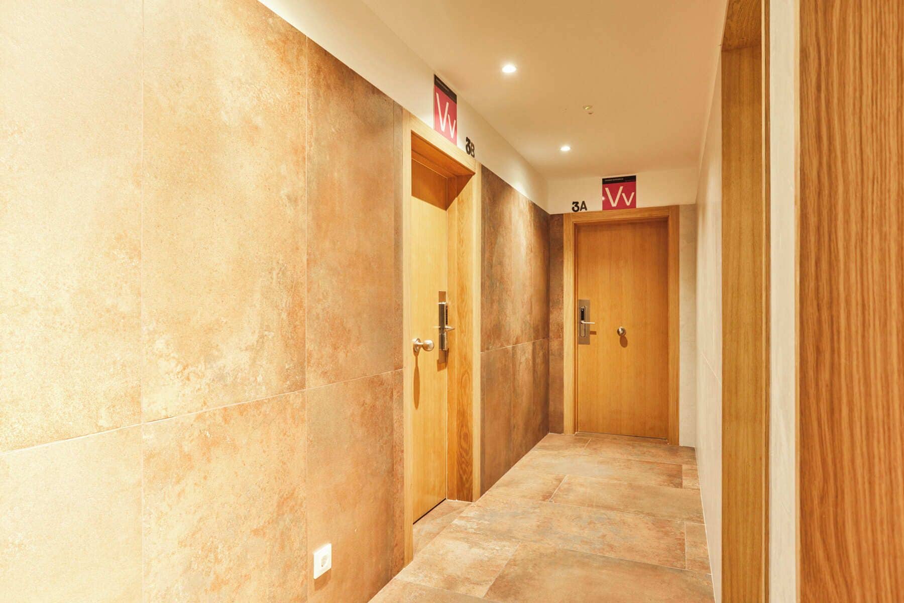 Un pasillo con paredes de mármol y puertas de madera, cada una con un número.