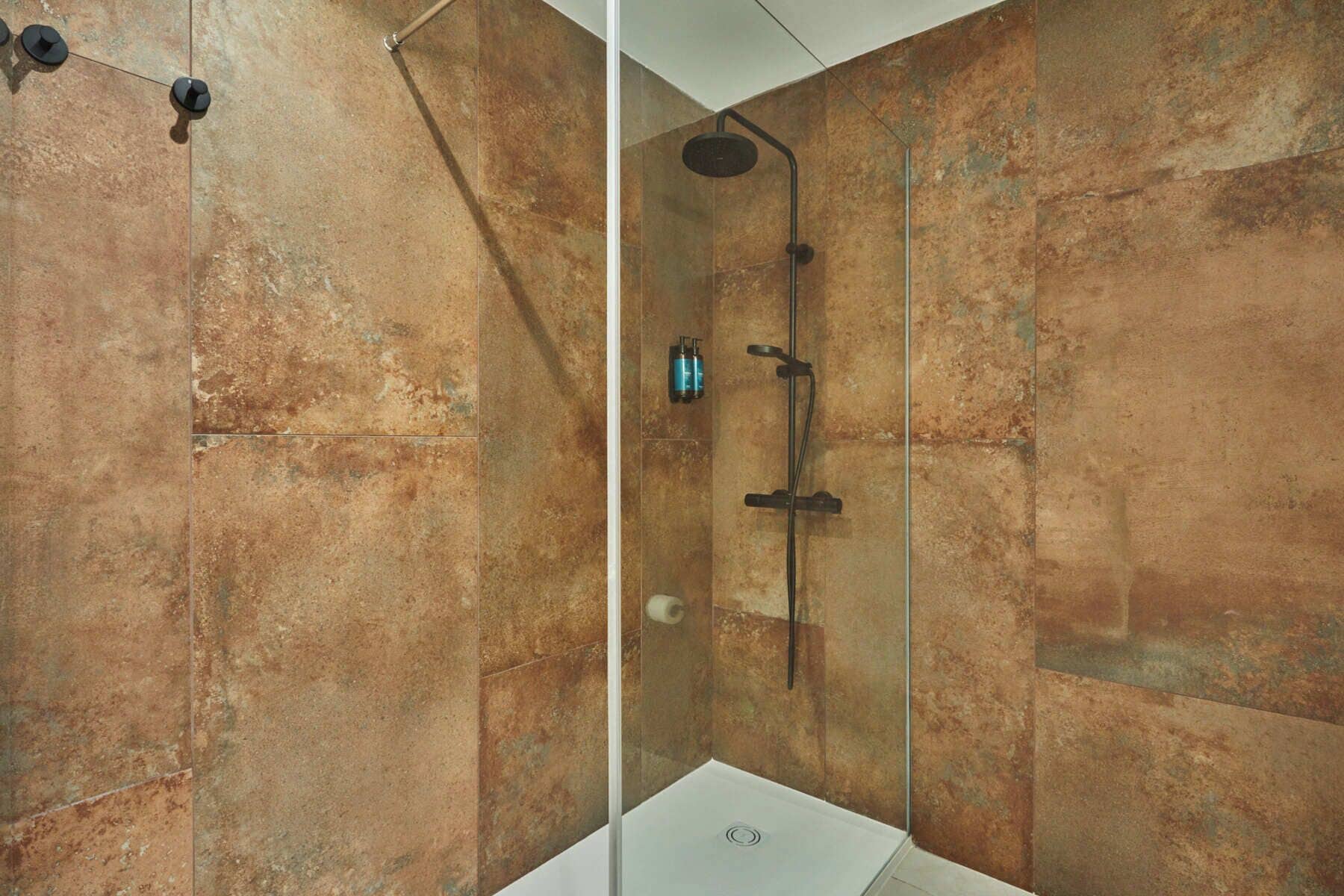 A shower with a glass door, a handheld showerhead, and a wall-mounted faucet.