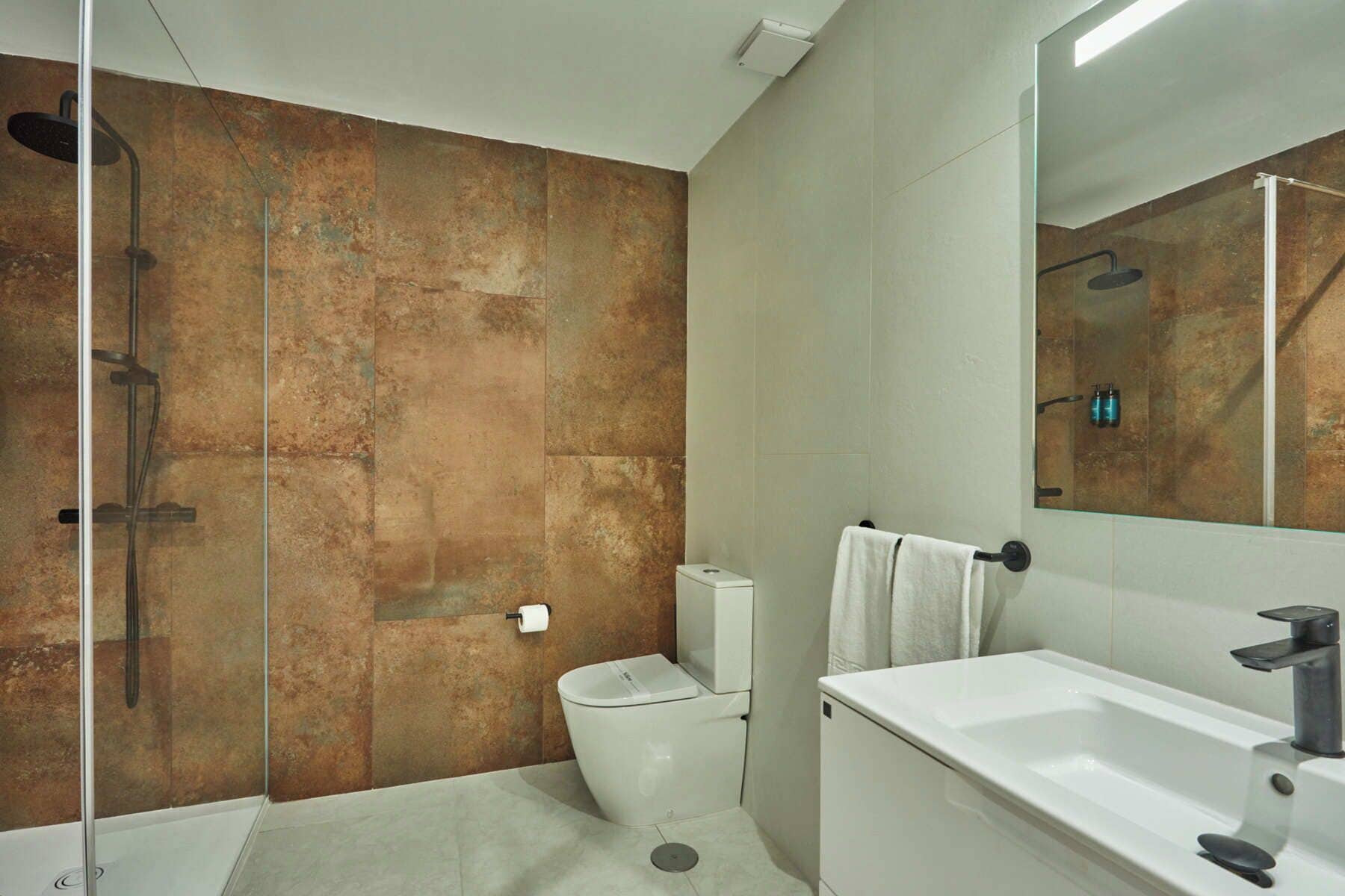Un baño moderno con ducha envuelta en vidrio, inodoro blanco y un espejo grande.