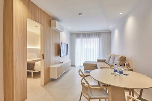 A modern hotel room with a wooden partition, a flat-screen TV, a sofa, a round table with chairs, and a large window with sheer curtains. - Silken Atlantis Playa – Holiday Homes (Las Palmas de Gran Canaria)