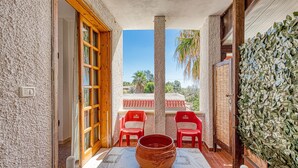 A patio with a table, chairs, and a large pot. There are red chairs, a wooden door, and a wall with green foliage. - Room in Guest Room - Studio Monolocale Margherita With Sea View, Balcony & Wi-fi (Salve)