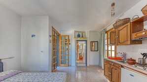 A bedroom with a bed, a bathroom with a sink, and a kitchen with wooden cabinets and a tiled floor. - Room in Guest Room - Studio Monolocale Margherita With Sea View, Balcony & Wi-fi (Salve)