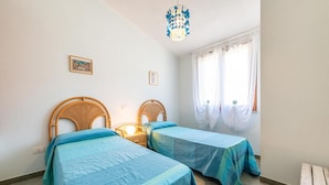 Ein Schlafzimmer mit zwei Einzelbetten, einem Nachttisch mit Lampe, einem Fenster mit Vorhängen und einem an der Wand hängenden Bild.