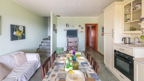A dining area with a table set for four, a sofa, a kitchen with an oven, and a staircase leading to another room. - Modern Villa Chia With Stunning sea View (Domus de Maria)