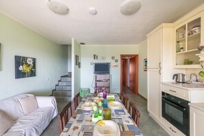 Un comedor con una mesa preparada para cuatro personas, un sofá, una cocina con horno y una escalera que lleva a otra habitación.