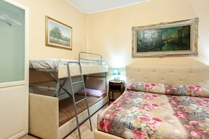 A bedroom with bunk beds, a bed with floral bedding, a nightstand, and two framed pictures on the wall. - Studio Near San Pietro (Rome)
