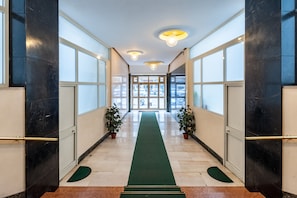 A hallway with a green carpet, black marble walls, and potted plants. - Studio Near San Pietro (Rome)