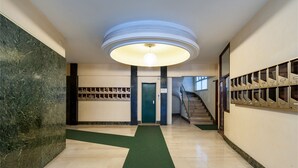 A hallway with a green carpet, a circular ceiling light, a green door, and a staircase. - Studio Near San Pietro (Rome)