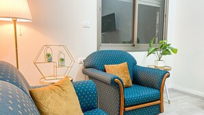 Ein Wohnzimmer mit einem blauen, gemusterten Sofa, einem Holzsesseln, einem kleinen Beistelltisch mit einer Pflanze und einer Lampe.
