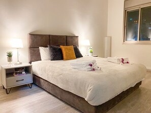 A neatly made bed with white linens, a brown headboard, and a bedside table with a lamp and a small plant. - Mary's Well 3 BR by Ahlan Hospitality (Nazareth)