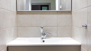 Ein Badezimmer mit einem weißen Waschbecken, einem Spiegel darüber und beige farbenen Fliesen an den Wänden.