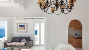 A spacious living room with a sofa, a coffee table, and a view of the sea through a large window. - Villa Panoramic Mykonos Near Nammos (Mykonos)