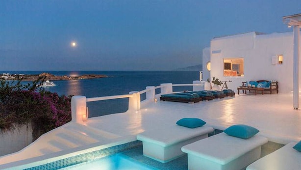 A modern outdoor pool area with lounge chairs and a view of the sea at dusk. - Villa Panoramic Mykonos Near Nammos (Mykonos)