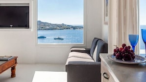 A living room with a large window offering a view of the sea and boats, a sofa, a coffee table with a plate of grapes, and a flat-screen TV mounted on the wall. - Villa Panoramic Mykonos Near Nammos (Mykonos)