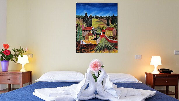 A hotel room with a bed, two bedside tables, a painting on the wall, and a vase with flowers on one of the tables. - Room-two-room Apartment (Arezzo)