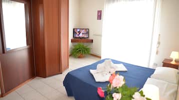 Una habitación de hotel con cama, televisión, planta en maceta y ventana con cortinas.