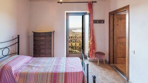 A bedroom with a bed, a dresser, a wooden door, and a view of the outdoors.