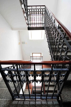 Uma escadaria com grades de metal preto ricamente decoradas e um corrimão de madeira.