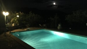 En swimmingpool om natten med måne i himlen.