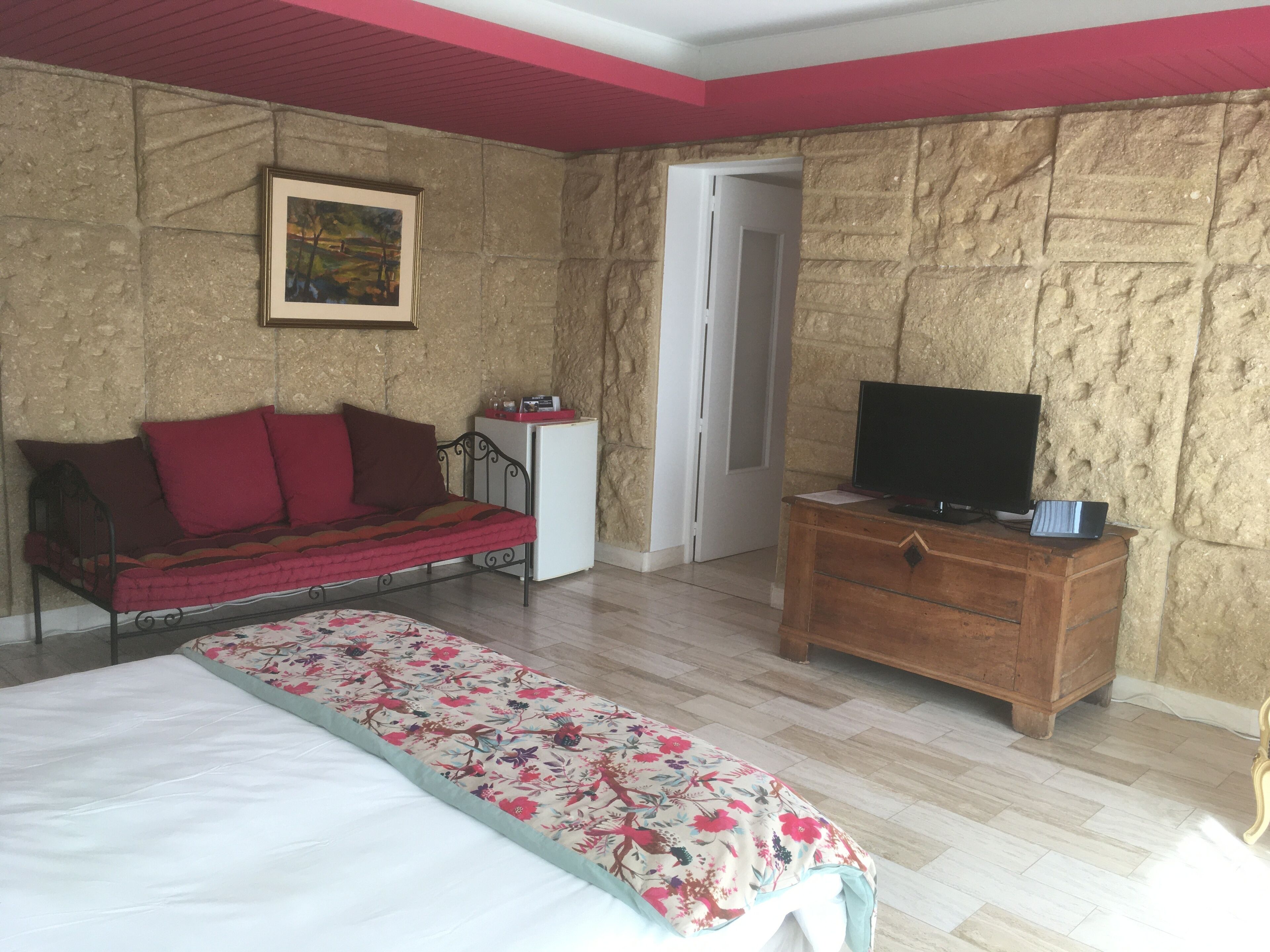 A bedroom with a bed, a sofa, a TV on a wooden dresser, and a door.