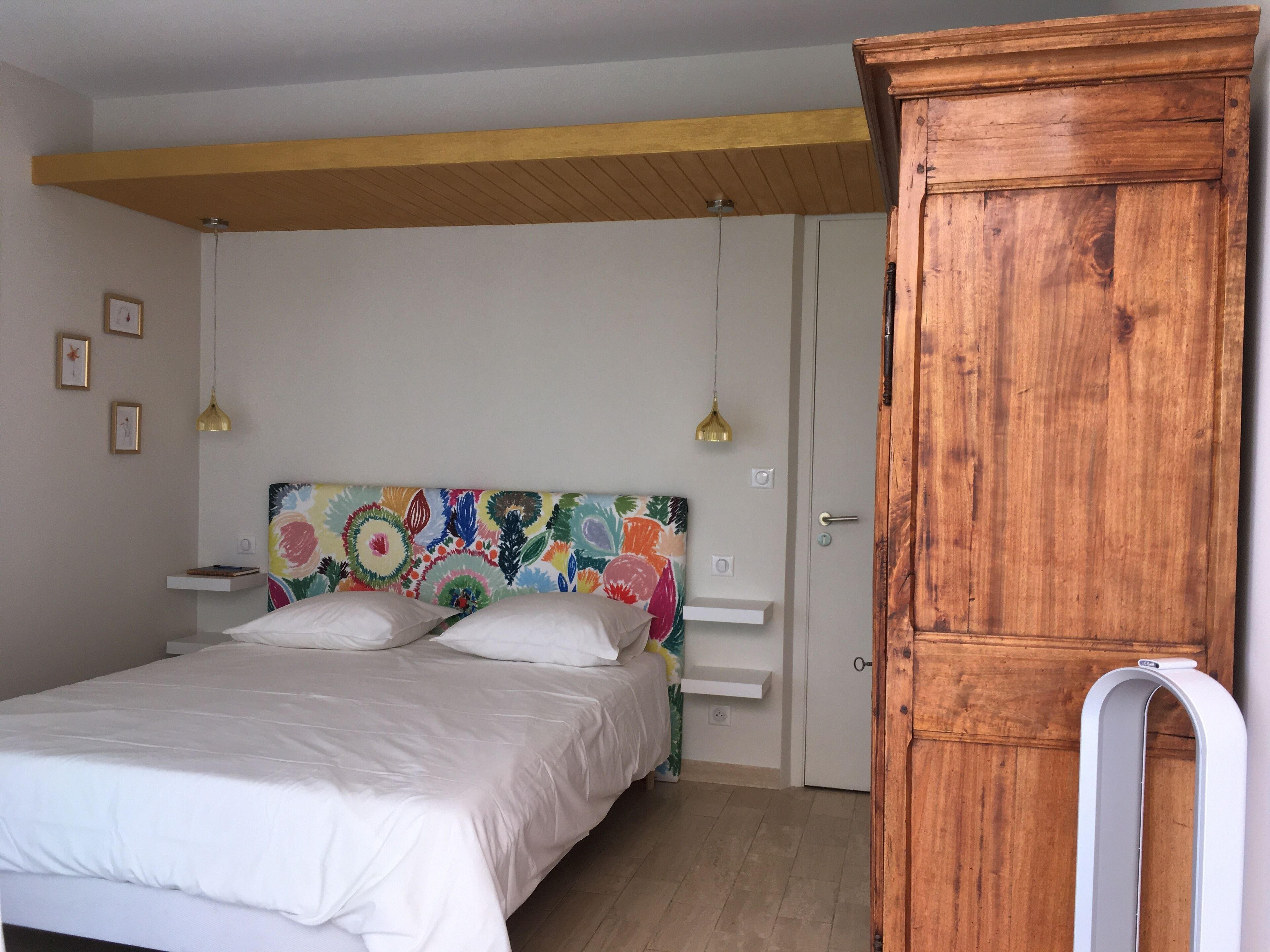 Un dormitorio con cama, un armario de madera, un cabecero colorido y una estantería blanca.