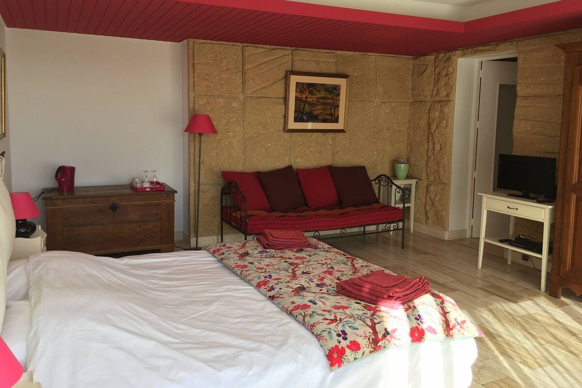 A bedroom with a bed, a sofa, a desk with a TV, a lamp, and a painting on the wall.