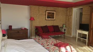 A bedroom with a bed, a sofa, a desk with a TV, a lamp, and a painting on the wall.