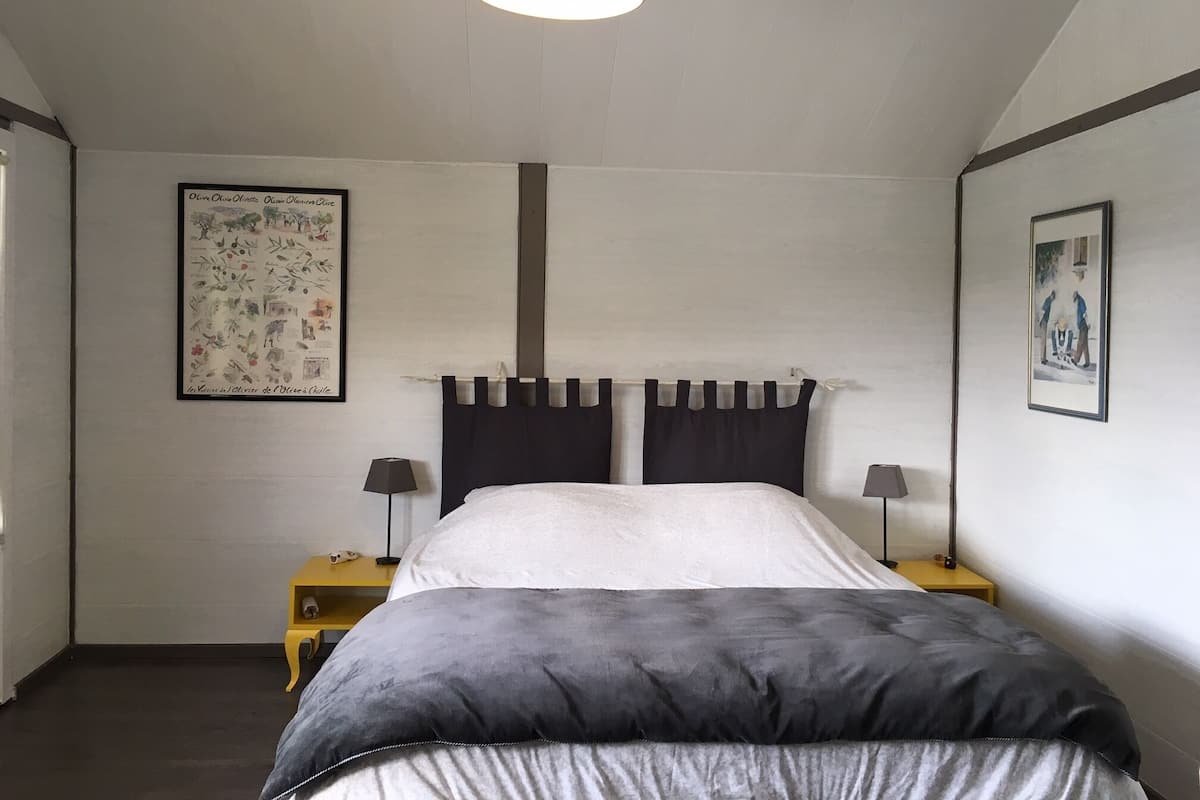 A bedroom with a bed, two bedside tables, a hanging lamp, and two framed pictures on the walls.