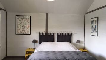 A bedroom with a bed, two bedside tables, a hanging lamp, and two framed pictures on the walls.