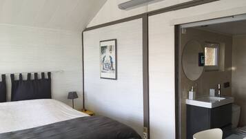 A bedroom with a bed, a bedside lamp, a framed picture on the wall, and a bathroom with a sink and mirror.