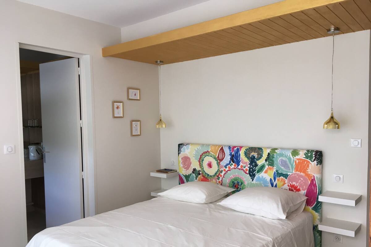 A bedroom with a bed, a wooden ceiling, a colorful headboard, and a white door.