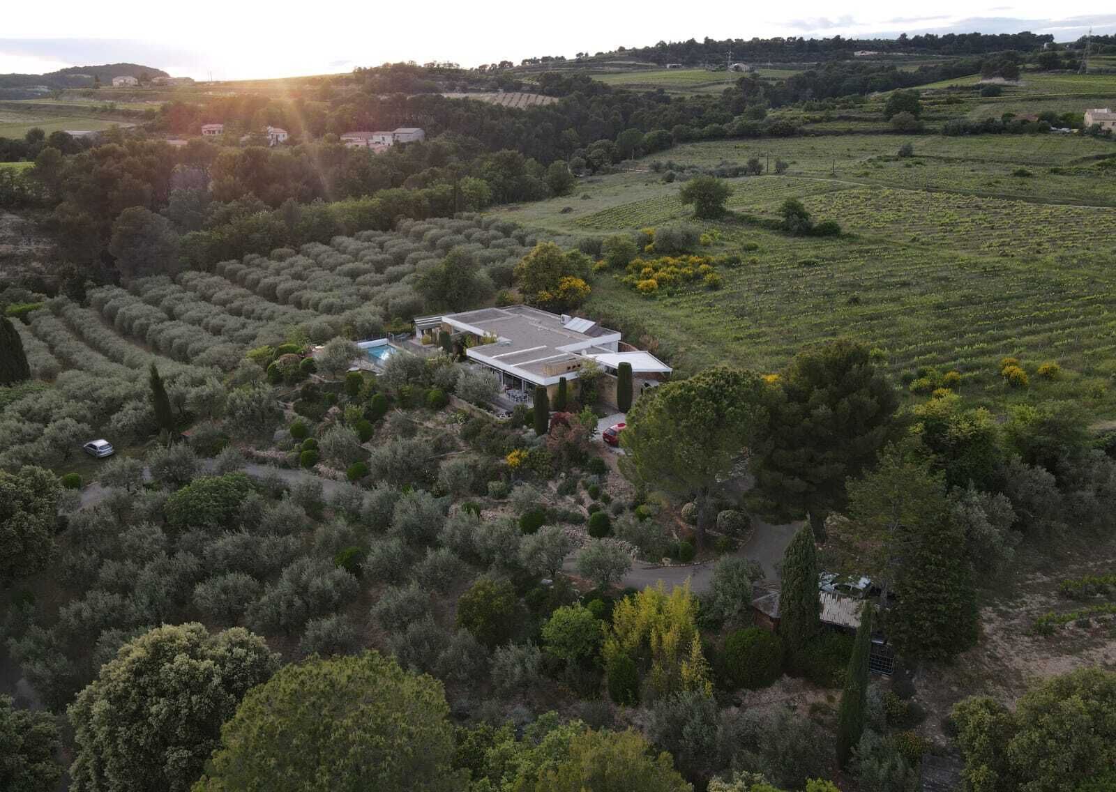 A large, modern building with a flat roof and large windows, surrounded by lush greenery and fields.