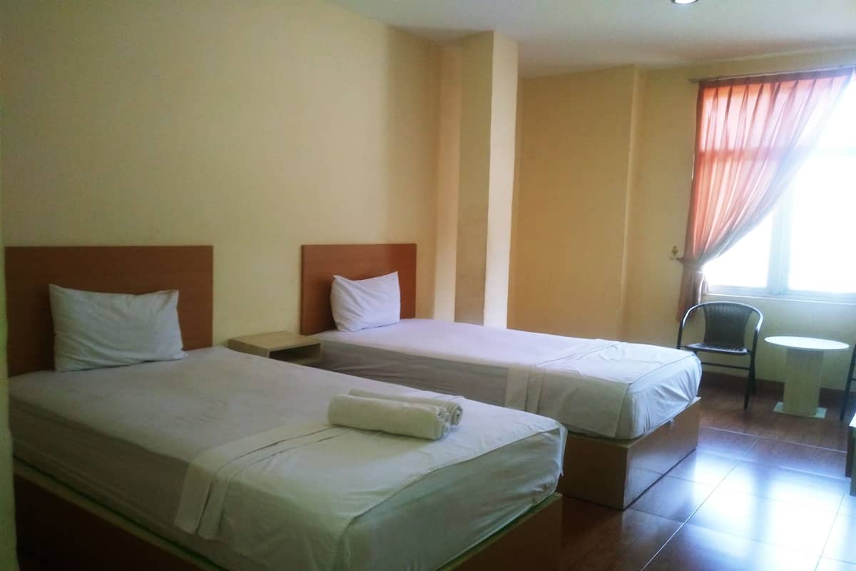 A hotel room with two single beds, a small table, and a chair.