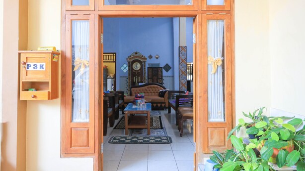 A room with a wooden door, a sofa, a coffee table, and a clock. - Hotel O Wallet Family Residence Syariah (Lumajang)