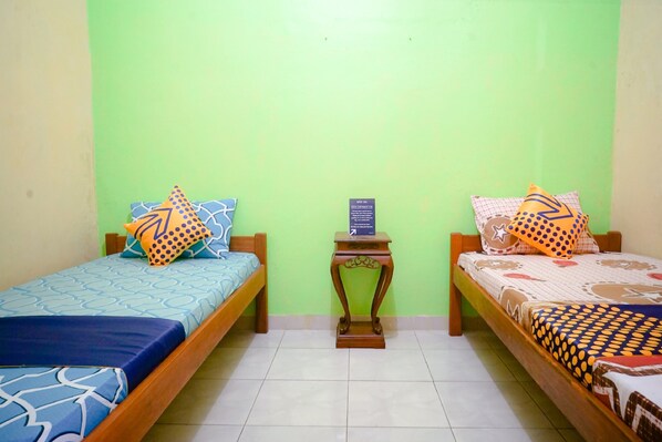 Una habitación con dos camas individuales, cada una con ropa de cama y almohadas estampadas. Hay una pequeña mesita de madera con un cartel entre las camas.