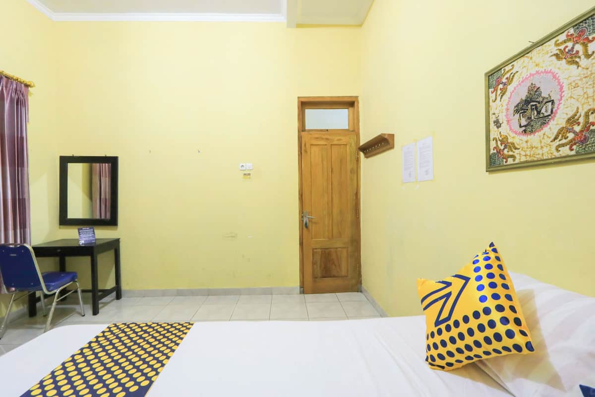 Une chambre d’hôtel comprenant un lit, un bureau, une chaise, une porte et une œuvre d’art accrochée au mur.