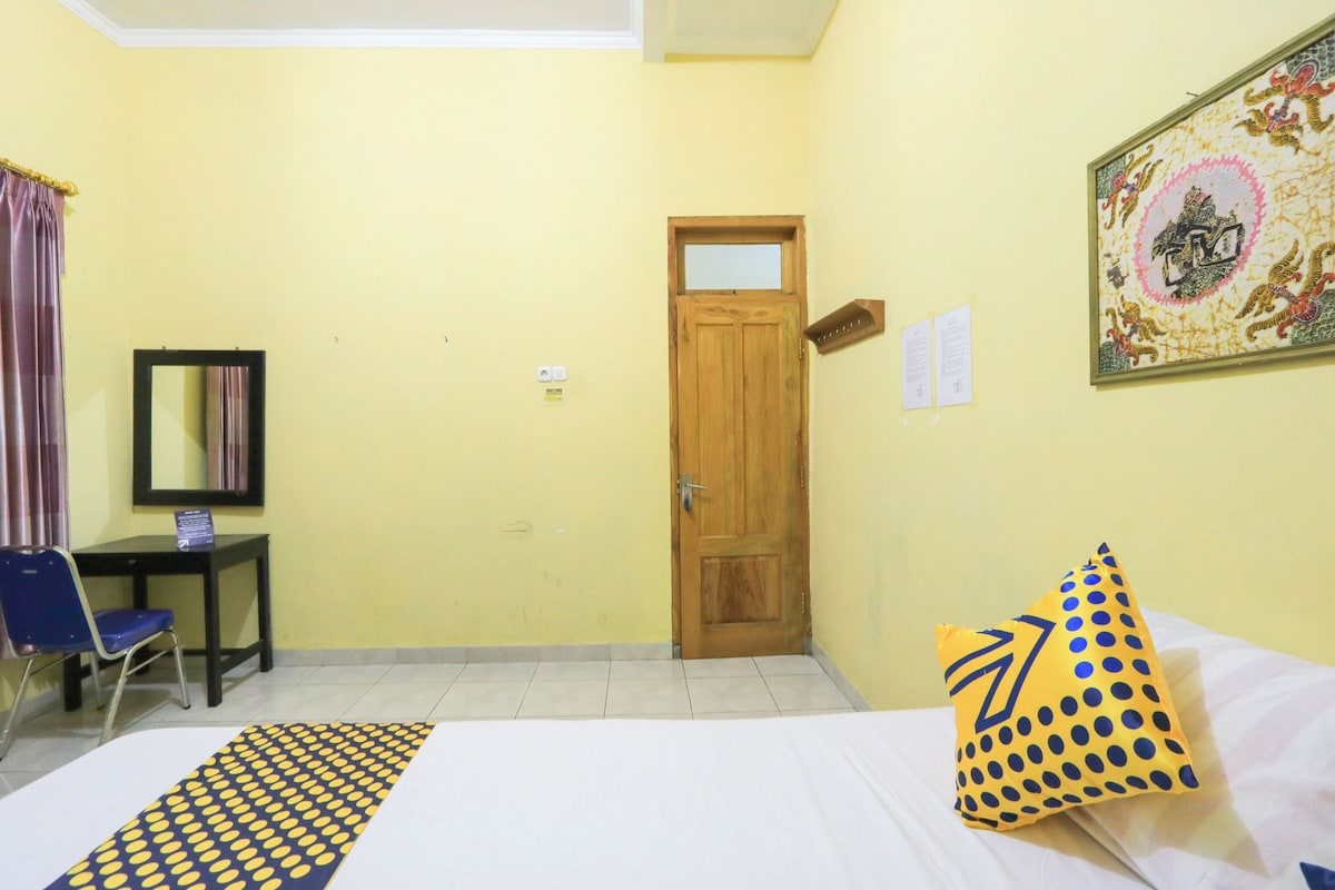 A hotel room with a bed, a desk, a chair, a door, and a wall-mounted artwork.