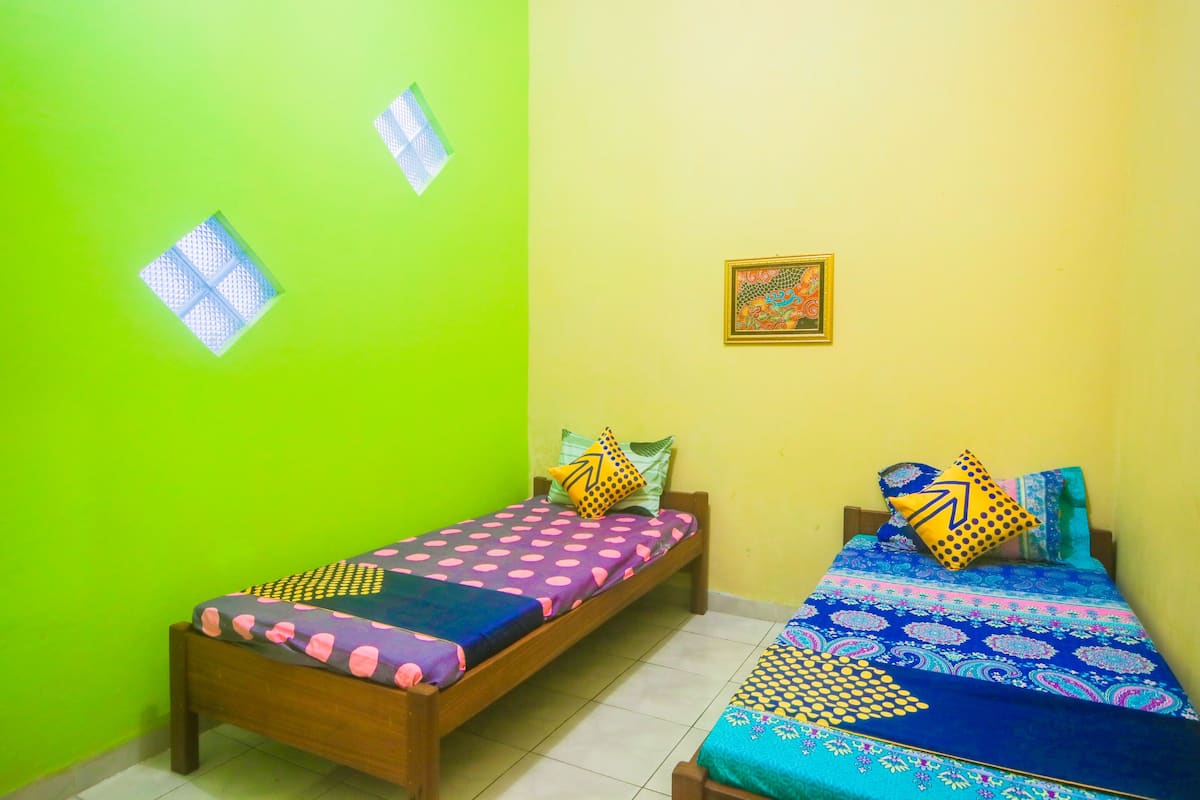 A room with two single beds, each with patterned bedding and pillows, against a green and yellow wall.
