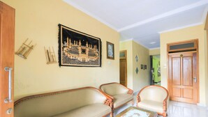 A living room with two sofas and a coffee table, a framed picture on the wall, and a wooden door in the background. - Hotel O Wallet Family Residence Syariah (Lumajang)