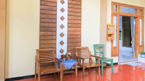 A wooden wall with a vertical panel and a door leading to a room. There are two wooden chairs and a small table with a blue tablecloth and a flower arrangement. - Hotel O Wallet Family Residence Syariah (Lumajang)
