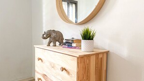Een houten dressoir met een spiegel, een klein olifantje, een bloempot en een paar boeken.