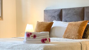 Een net opgemaakt bed met een witte dekbedovertrek, meerdere kussens en een decoratieve bloemstelling.