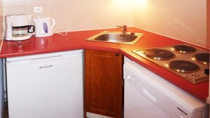 Una cocina compacta con armarios de madera, encimera roja, microondas integrado, cafetera, lavaplatos y lavabo.