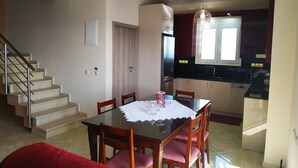 A dining area with a glass table, wooden chairs, and a red sofa. A staircase is visible to the left, and a kitchen with dark cabinets and a window is to the right. - Luxurious Villa Paradise PRIVATE BEACH (Faistos)