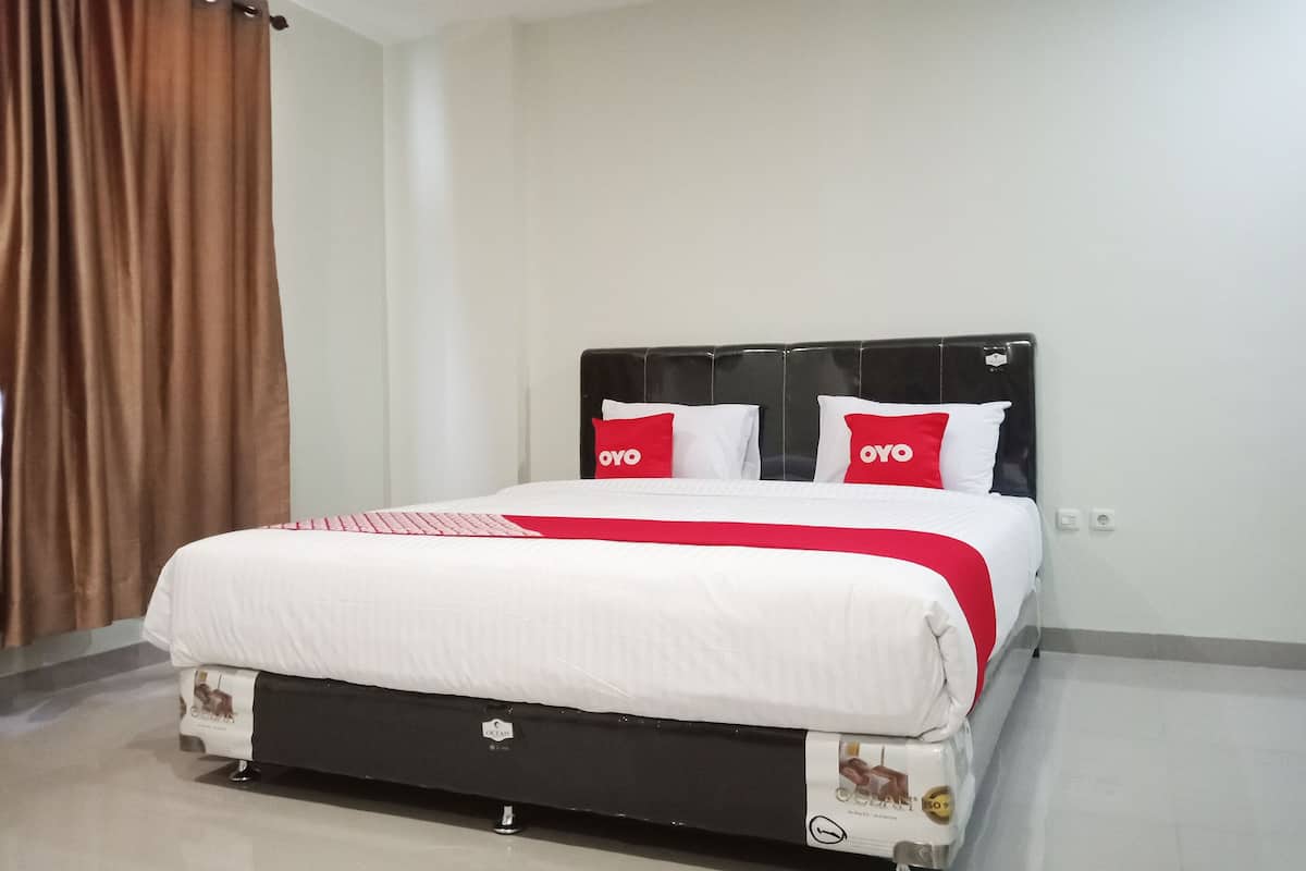 A neatly made bed with a white and red bedspread, two pillows with the 'OYO' logo, and a black headboard.