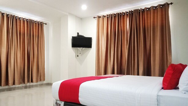 A hotel room with a bed, curtains, a mounted TV, and a red pillow. - OYO 2382 Wisata Hotel (Samosir)