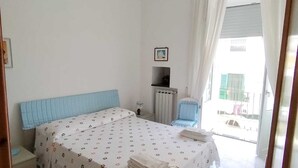 A bedroom with a bed, a radiator, a chair, and a window with curtains. - Ischia Ponte Romantic Apartment in the Historical Center and Near the sea (Ischia)